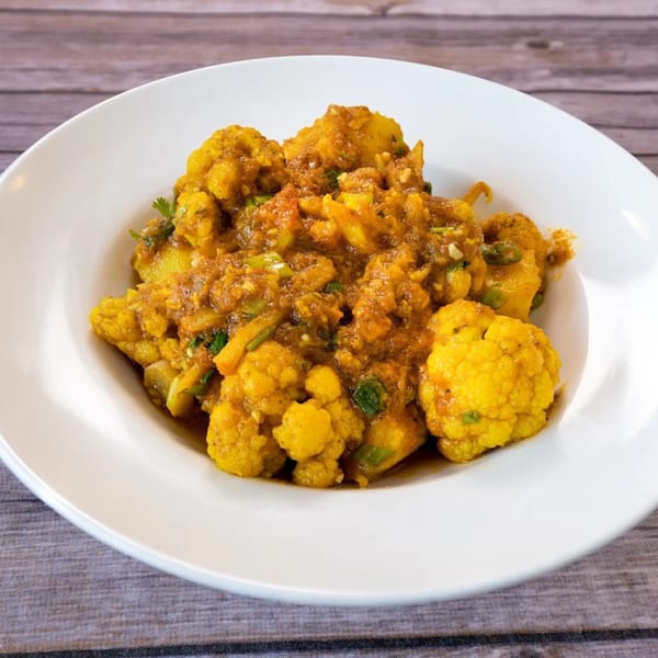 A white bowl filled with vibrant yellow Indian cauliflower and potato curry, garnished with green herbs.