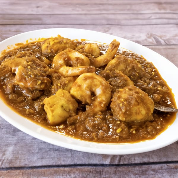 A white oval plate filled with Bengal Tiger's shrimp and potato curry in a rich, brown sauce.