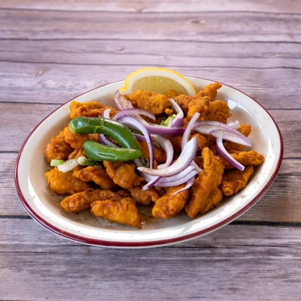 Indian chicken pakora with red onions, green chilies, and a lemon wedge on a white plate.