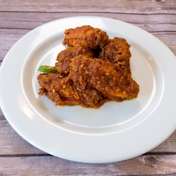 Spicy Indian chicken wings, coated in a rich red sauce, garnished with green chili slices.