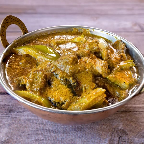Indian curry with green peppers and meat in a traditional copper serving bowl on a wooden table.