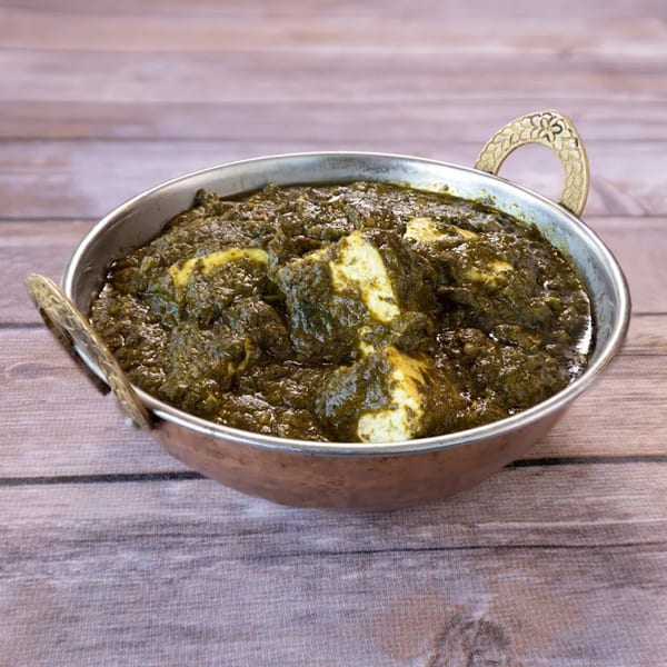 A copper karahi bowl filled with vibrant green Indian palak paneer on a wooden surface.